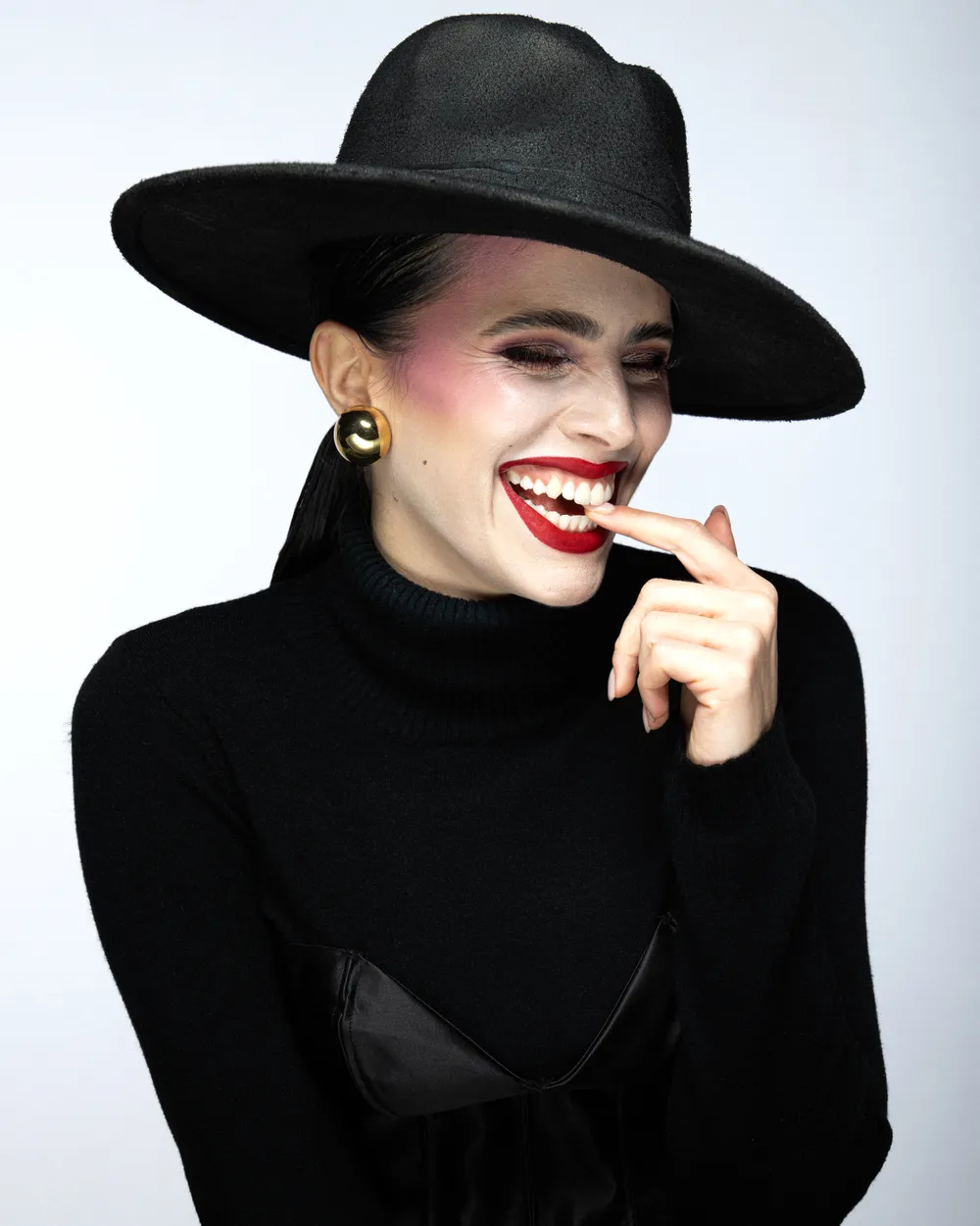 Cappello a falda larga e dolcevita nero, orecchini a sfera, in studio.